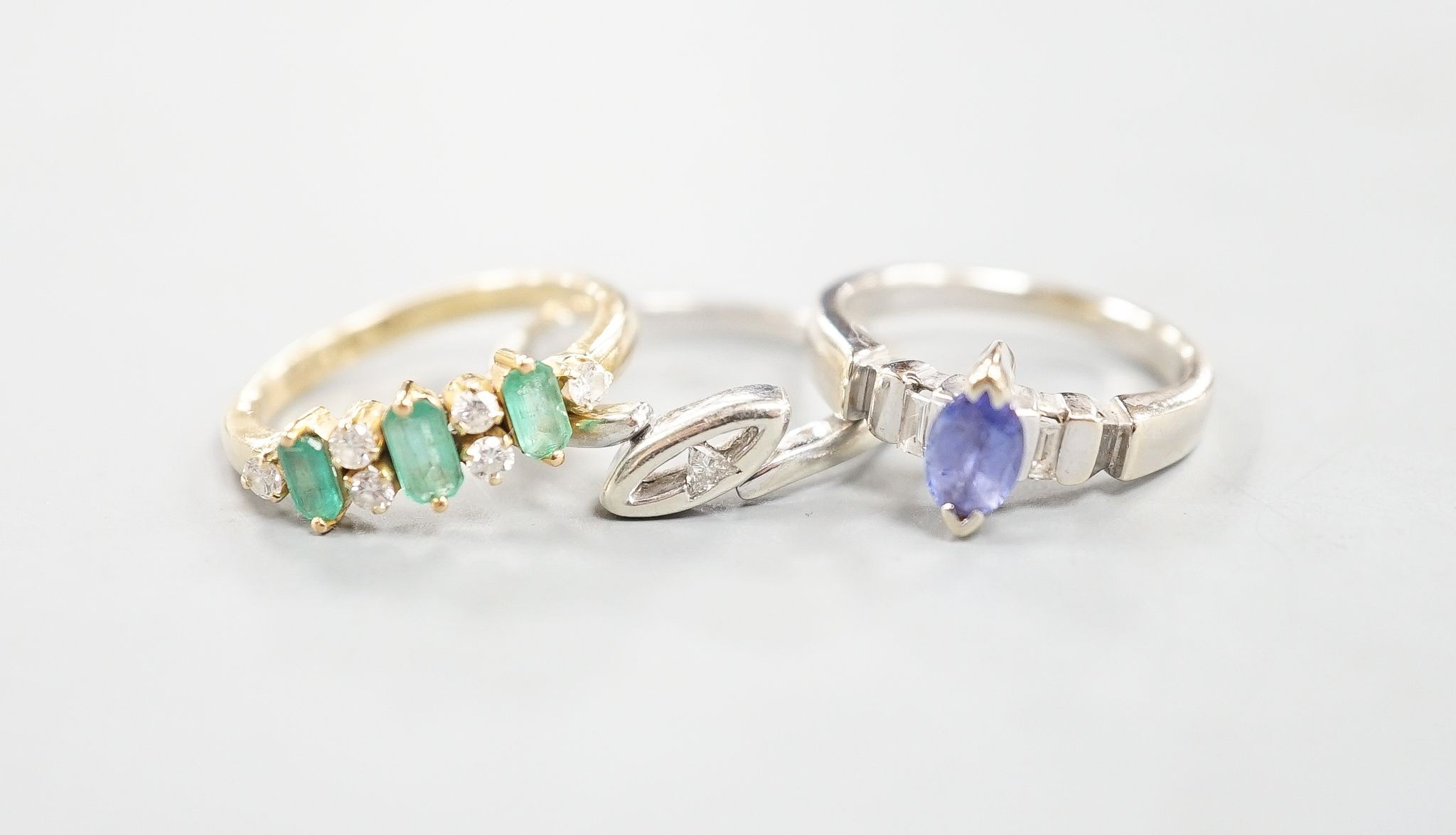 A 750 yellow metal, three stone emerald and six stone diamond chip set half hoop ring, size L, a 750 white metal and tanzanite ring, size K, gross 6.4 grams and a 9ct white gold and diamond chip set ring, gross 2.4 grams